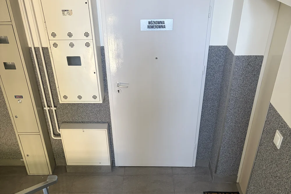 Odnowione drzwi wózkowni i rowerowni obok szaf instalacyjnych na klatce schodowej