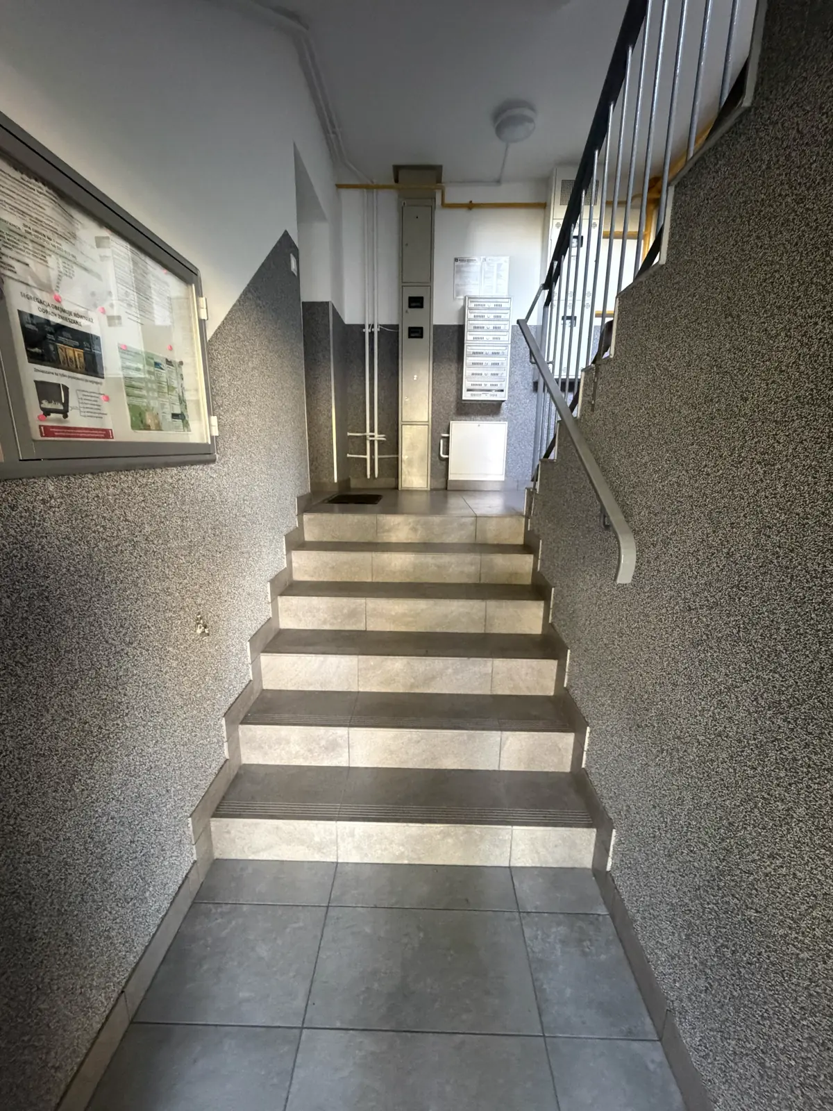 Widok klatki schodowej po modernizacji z nowymi stopniami gresowymi i szarą lamperią