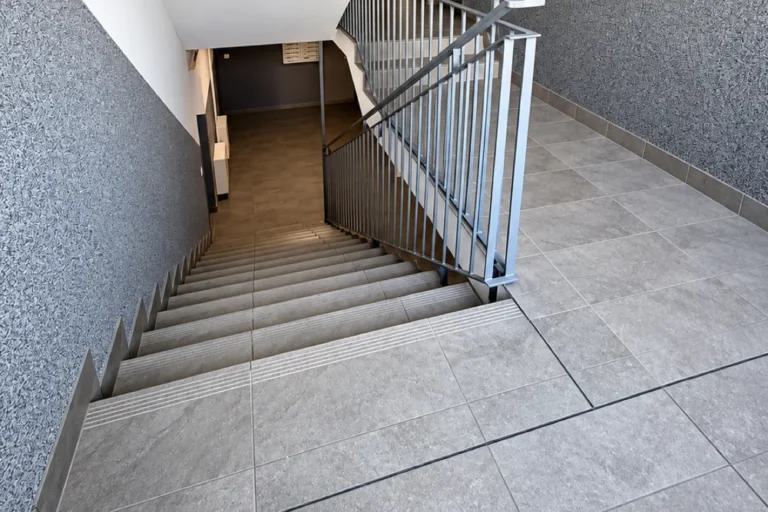Schody z szarym gresem, balustradą i lamperią mozaikową po modernizacji klatki schodowej