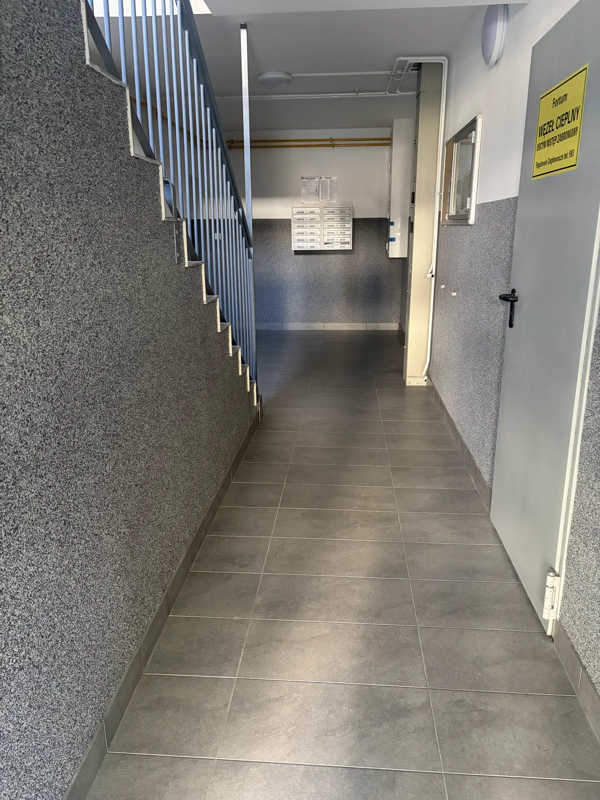 Korytarz klatki schodowej po remoncie z nową posadzką gresową i szarą lamperią