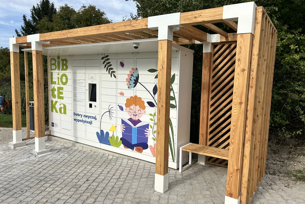 Pergola z drewnianą ścianą ażurową i ławką przy książkomacie